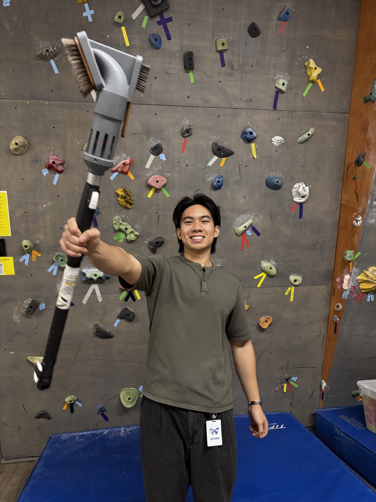 Reagan holding the finished brush on its extendable pole at the climbing wall